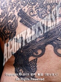 背中に拳銃（ピストル）と英文字のタトゥー画像【エゴニー アンド エクスタシー タトゥーデザインスタジオ】彫迫